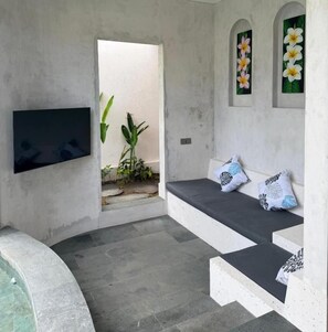 Ein Zimmer mit einem wandmontierten Flachbildfernseher, einer Sitzecke mit Kissen und einer kleinen Wasserspende.