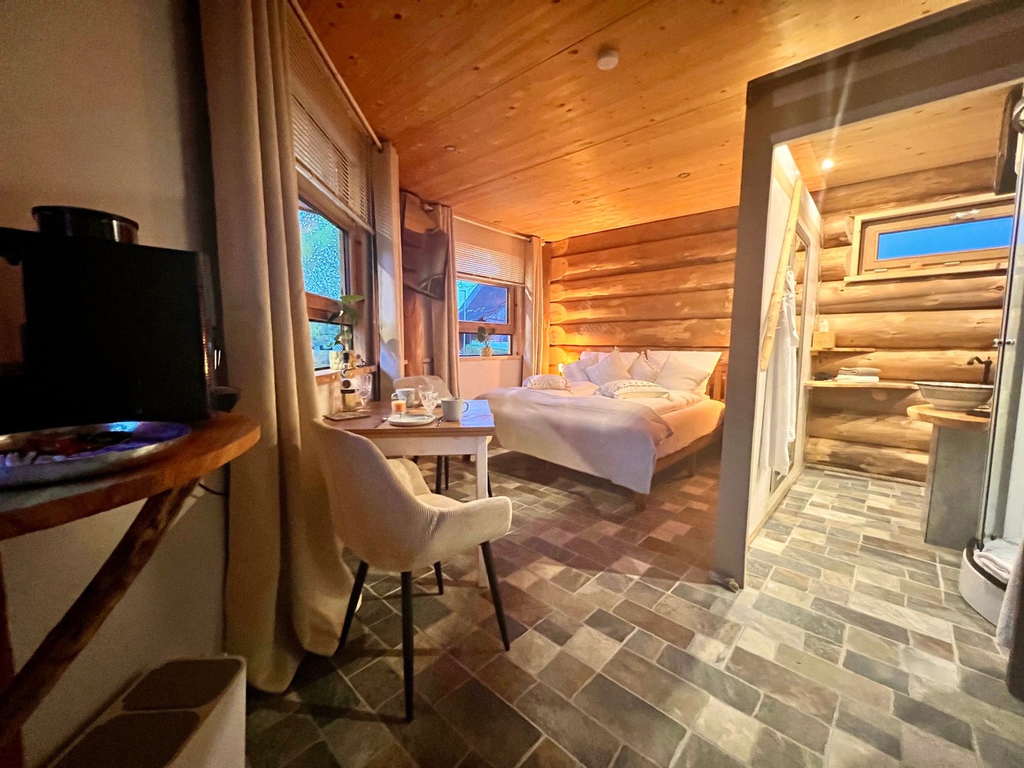 A cozy log cabin room with a bed, a dining table, and a television.