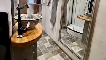 Ein Badezimmer mit einem Holzkosmetikschrank, einem großen Spiegel, einer Duschkabine und einem gefliesten Boden.