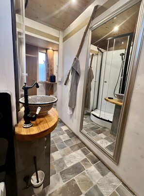 Une salle de bain avec un meuble-lavabo en bois, un grand miroir, un espace douche et un sol carrelé.