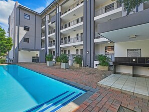 A multi-story building with a swimming pool, outdoor seating, and a signboard. - Regentis Executive Stays at The Atrium unit 163 (City of Johannesburg Metropolitan Municipality)