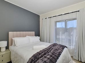 A bedroom with a bed, a bedside table, and a window with curtains. - Regentis Executive Stays at The Atrium unit 163 (City of Johannesburg Metropolitan Municipality)