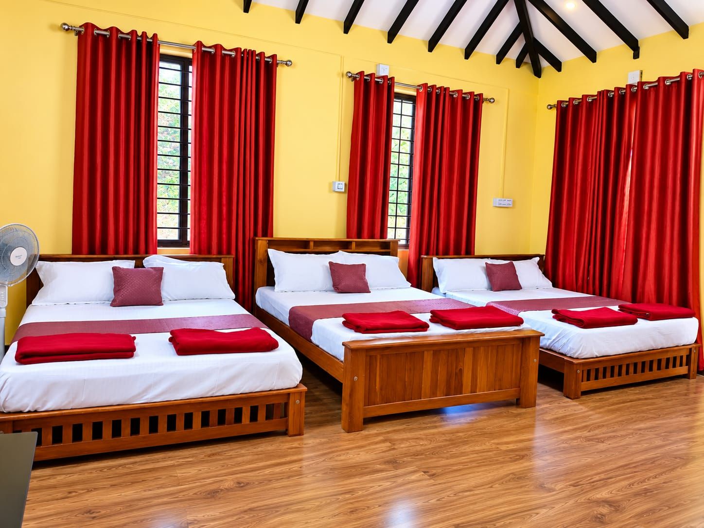 A hotel room with three wooden beds, red curtains, and a fan.