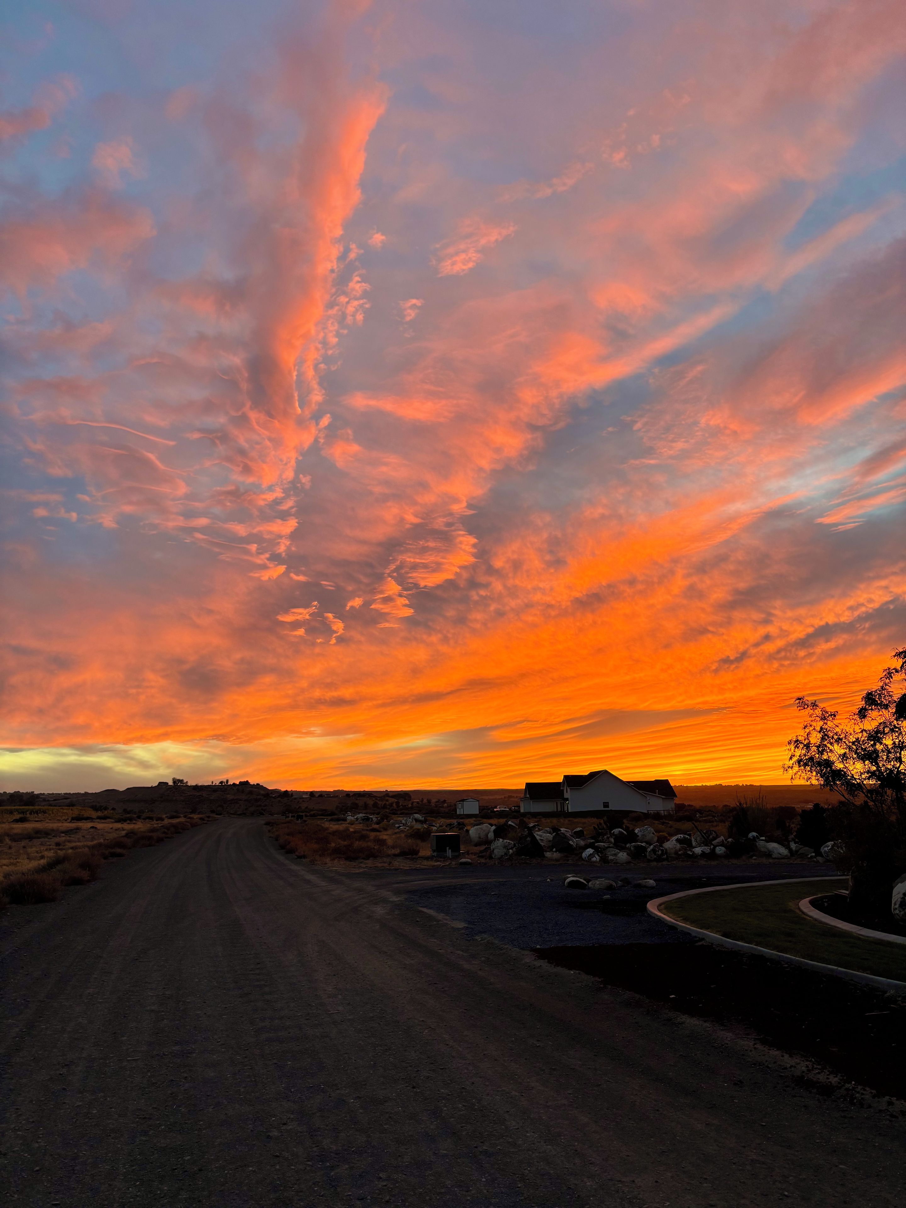 Eine ländliche Straße führt zu einer Ansammlung von Gebäuden unter einem Sonnenuntergangshimmel.