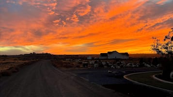 Eine ländliche Straße führt zu einer Ansammlung von Gebäuden unter einem Sonnenuntergangshimmel.