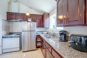 Una cocina con refrigerador de acero inoxidable, estufa a gas, gabinetes de madera, encimeras de granito y una cafetera.