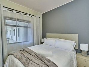 Una habitació d'hotel amb un llit, una làmpada de nit i una finestra amb cortines.