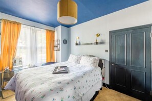 Ein Schlafzimmer mit einem Bett, einem Schreibtisch, einem Stuhl, einem Kleiderschrank und einem Fenster mit Vorhängen.