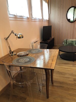 A dining area with a wooden table, clear chairs, a metal lamp, and a round black table. - Le Bicoquet in Caen: An Elegant and Cozy Apartment (Caen)