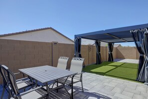 A patio with a table and chairs, a covered area, and a brick wall. - Pool & Hot Tub Access! Goodyear Extended Escape (Goodyear)