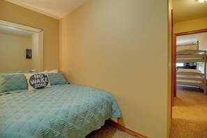 A bedroom with a bed, a wall-mounted mirror, and a bunk bed in the adjacent room. - Grand Lake Escape: Deck, Hot Tub, Views! (Eucha)