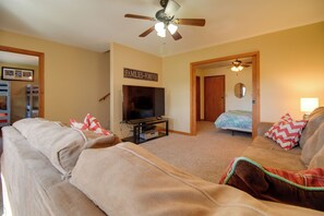 A living room with a television, a ceiling fan, and a door leading to another room. - Grand Lake Escape: Deck, Hot Tub, Views! (Eucha)