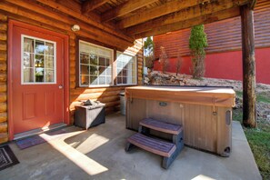 A wooden cabin with a red door, a hot tub, and a small outdoor seating area. - Grand Lake Escape: Deck, Hot Tub, Views! (Eucha)