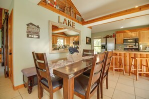 A wooden dining table with chairs, a kitchen with wooden cabinets, and a large mirror above the table. - Grand Lake Escape: Deck, Hot Tub, Views! (Eucha)