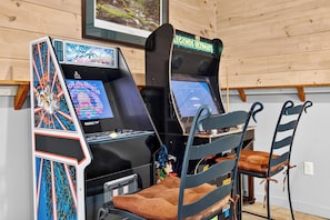 Ein Spielhallenambiente mit zwei Spielautomaten, einem braunen Sitzhocker und einer Holzwand.