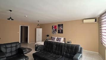 A living room with a sofa set, a coffee table, and a TV. There is a door leading to another room and a window with blinds.