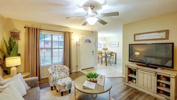 A living room with a ceiling fan, a television, a dining area, and a door leading to another room.