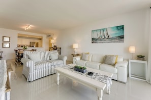 A modern living room with a striped sofa, a white sofa, a coffee table, and a painting of sailboats on the wall. - Resort Condo w/ Views in Sunny Isles Beach! (Sunny Isles Beach)