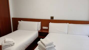 Una habitación de hotel con dos camas individuales, cada una con ropa de cama y almohadas blancas, y un cabecero de madera. Hay una mesita de noche de madera entre las camas con un enchufe.