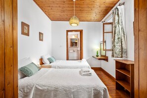 A room with two beds, a wooden ceiling, a hanging light fixture, a mirror, and a window with curtains. - Phaedrus Living: Lania Traditional Cottage (Laneia)