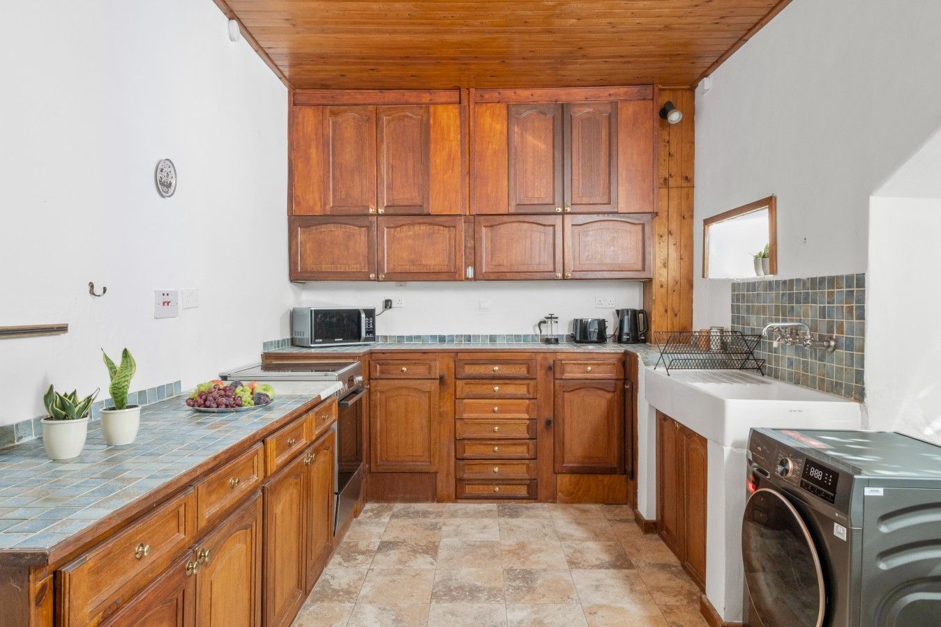 A compact kitchen with wooden cabinets, a microwave, a coffee maker, and a washing machine.