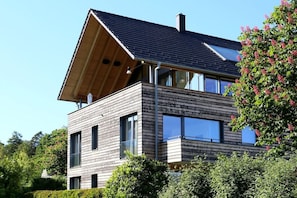 A modern two-story house with a sloped roof, large windows, and a wooden facade. - Holiday apartment with 2 bedrooms (Bodolz)