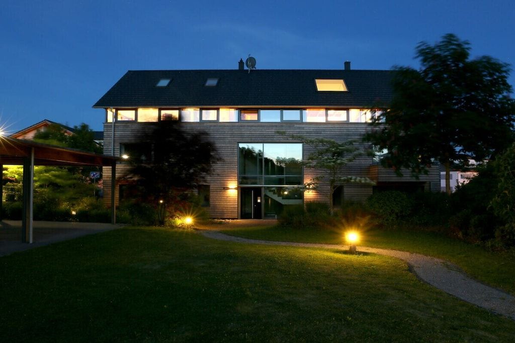 Ein modernes, zweistöckiges Haus mit Flachdach, großen Fenstern und einer gut beleuchteten Eingangsparte.