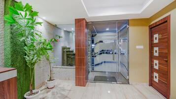 Un vestíbulo de hotel con mostrador de recepción, plantas en macetas, puerta de cristal de entrada y una escalera que conduce a pisos superiores.