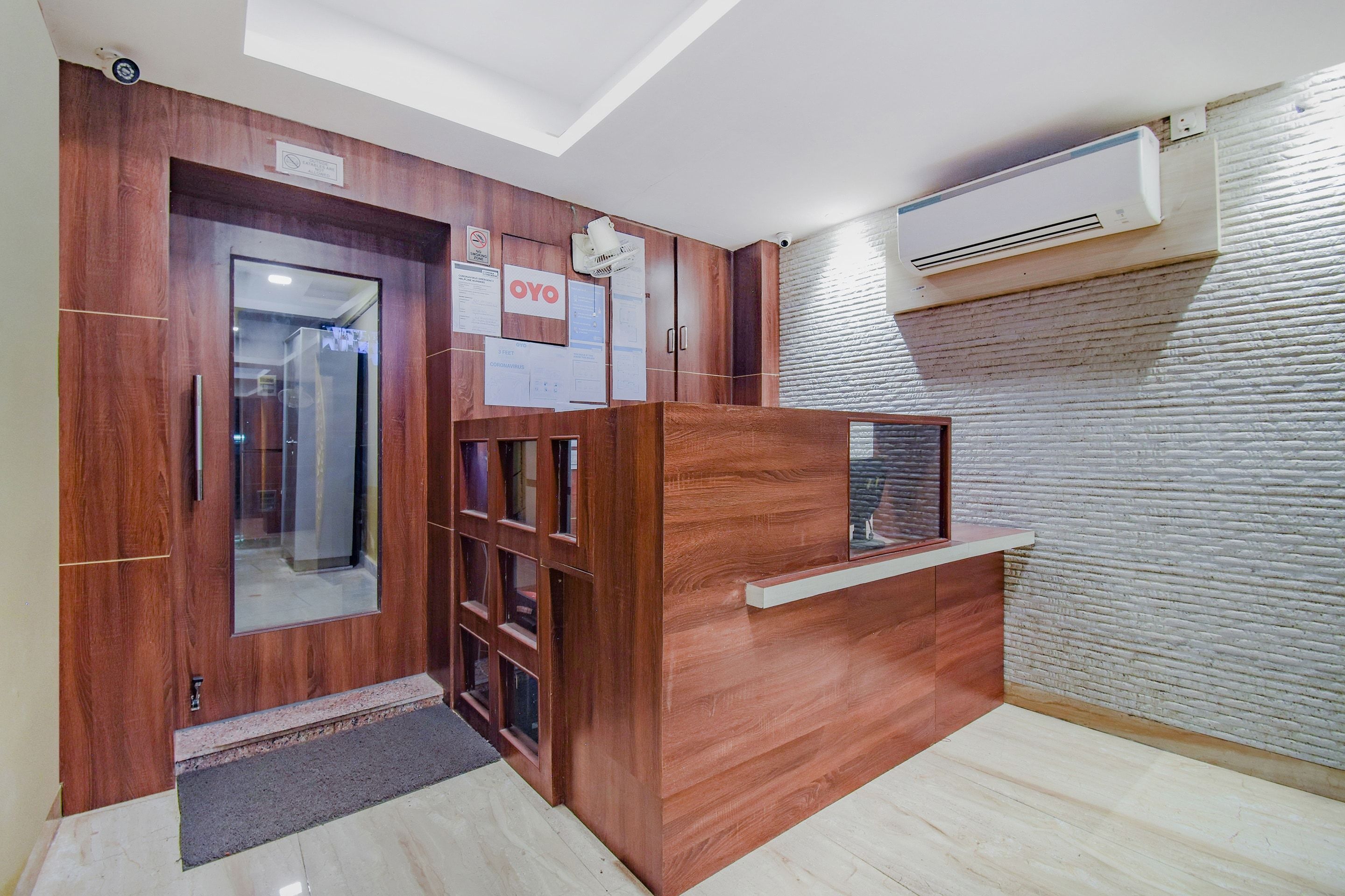 Zona de recepción con mostrador de madera, separador de vidrio y señalización sobre medidas de seguridad por COVID-19.