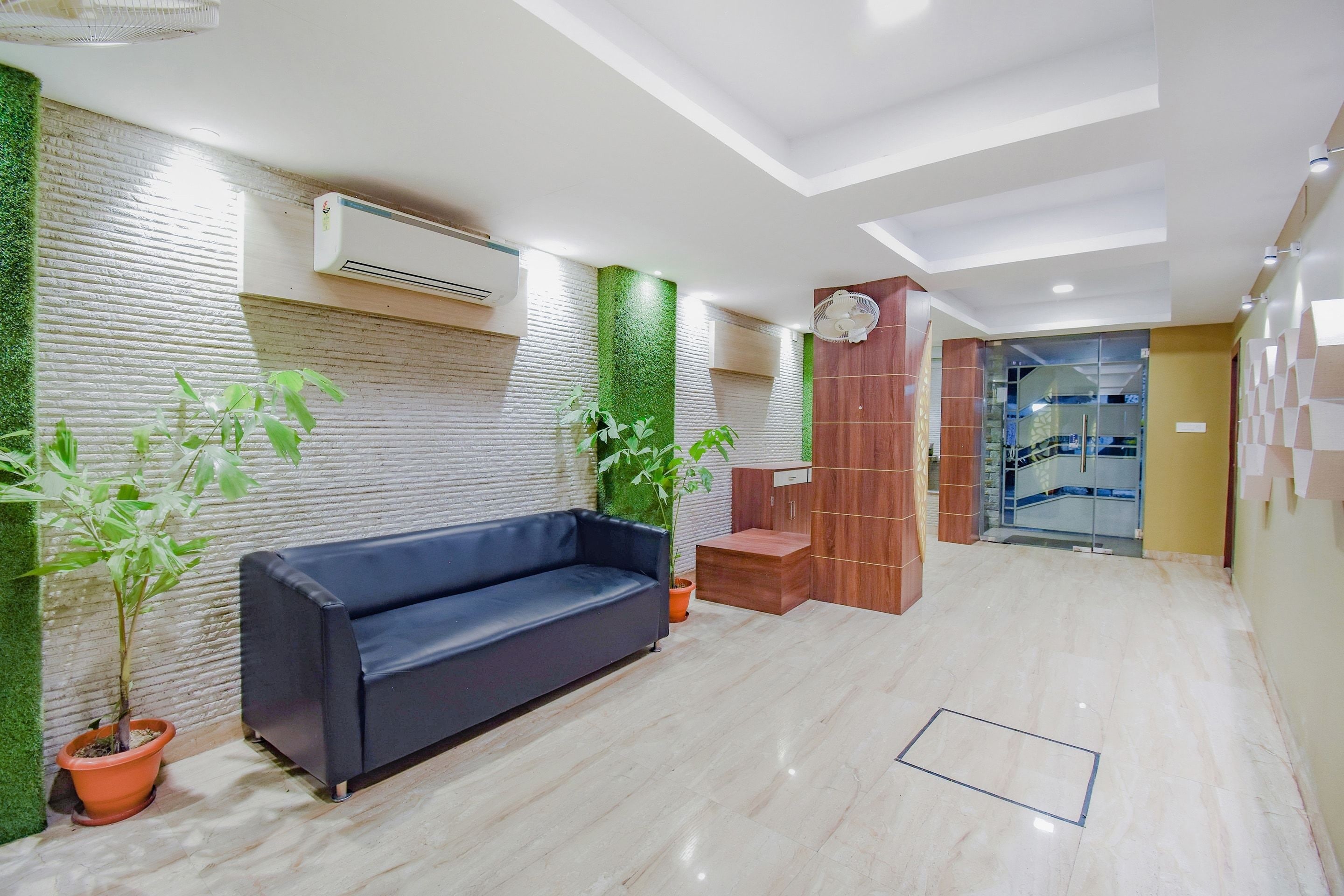 A modern lobby with a blue sofa, green plants, a wooden cabinet, and a glass staircase.