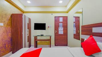 Una habitación de hotel con cama, escritorio, televisor y dos puertas.