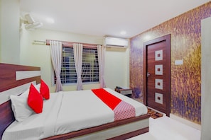Quarto de hotel com cama, cortinas, aparelho de ar condicionado, porta de madeira e parede estampada.