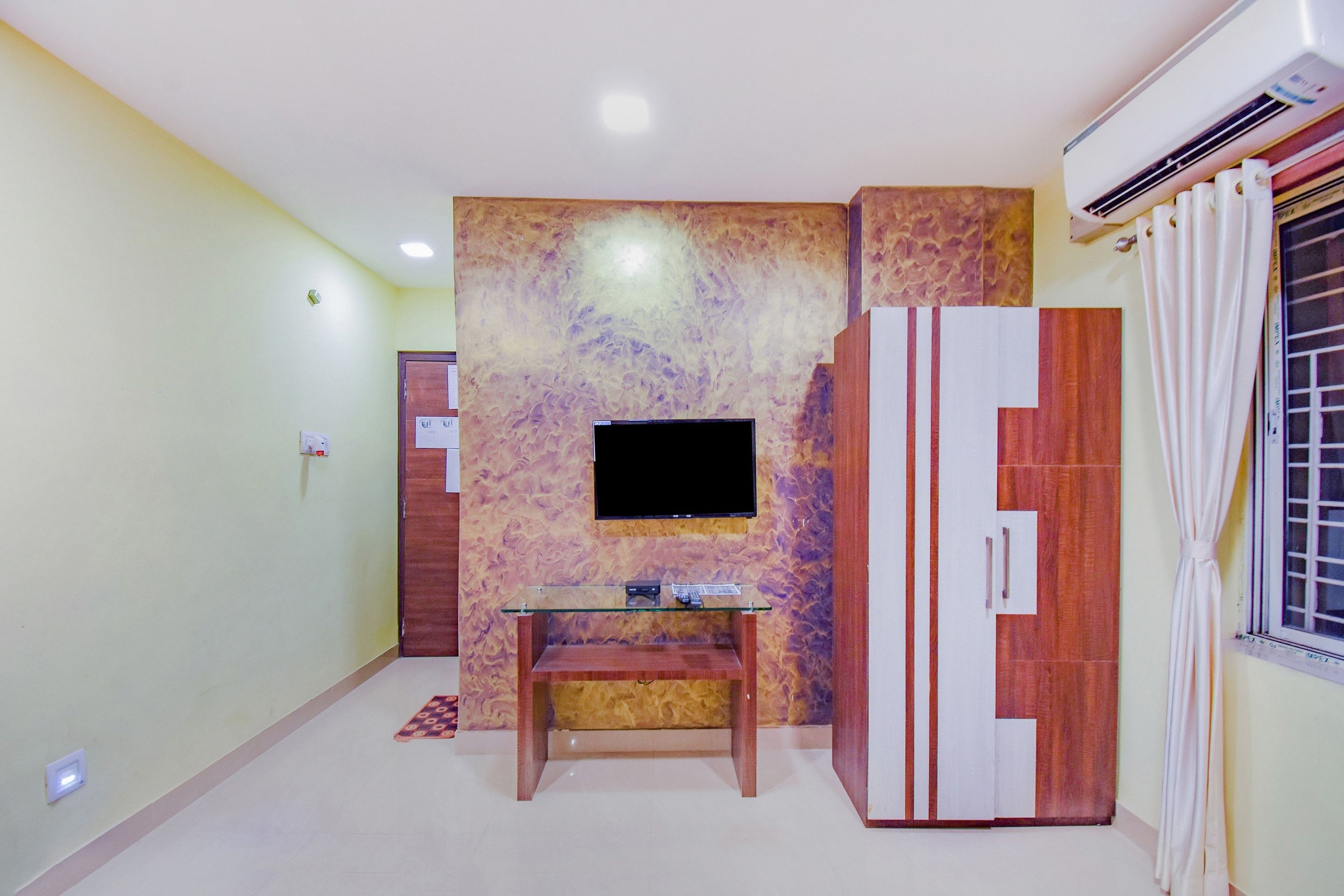Una habitación con televisión de pantalla plana en una pared con textura, un mueble de madera con espejo y una mesita con control remoto.