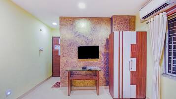 Una habitación con televisión de pantalla plana en una pared con textura, un mueble de madera con espejo y una mesita con control remoto.