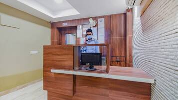 Un mostrador de recepción con un monitor de computadora, paneles de madera y un letrero que indica una distancia social de aproximadamente 90 centímetros.