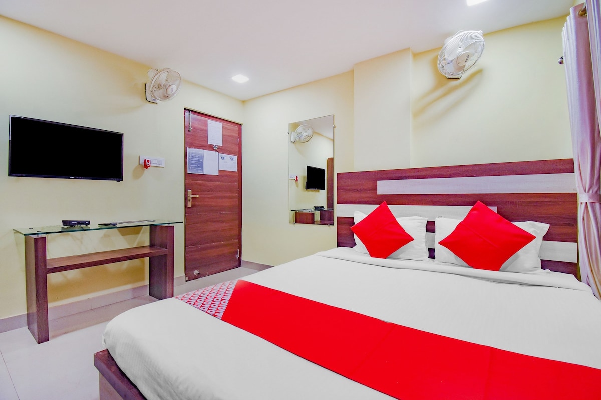 Quarto de hotel com cama, escrivaninha, televisão e porta.