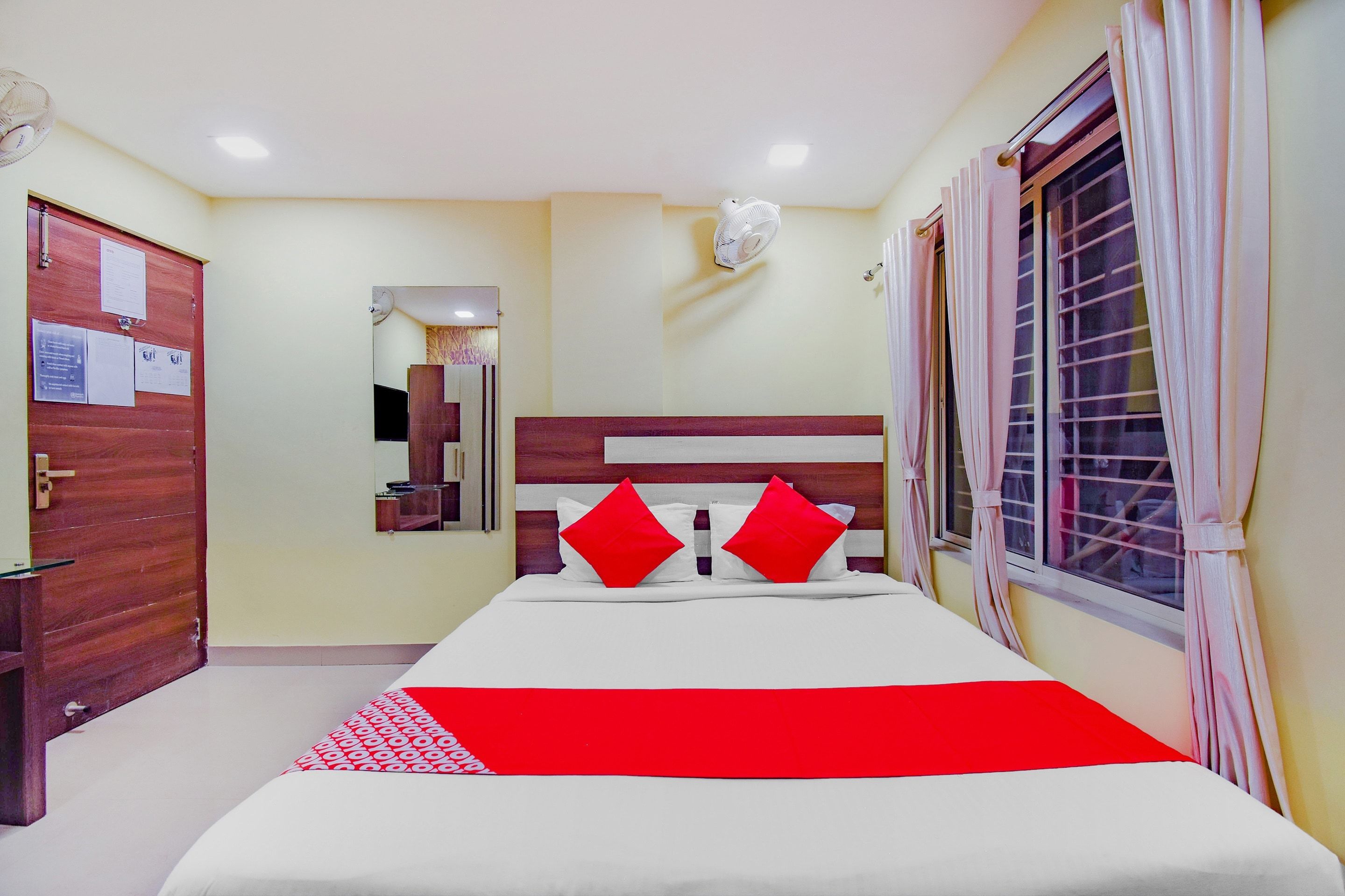 Una habitación de hotel con cama, espejo, ventana con cortinas y puerta.