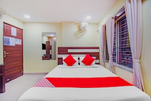 Quarto de hotel com cama, espelho, janela com cortinas e porta.