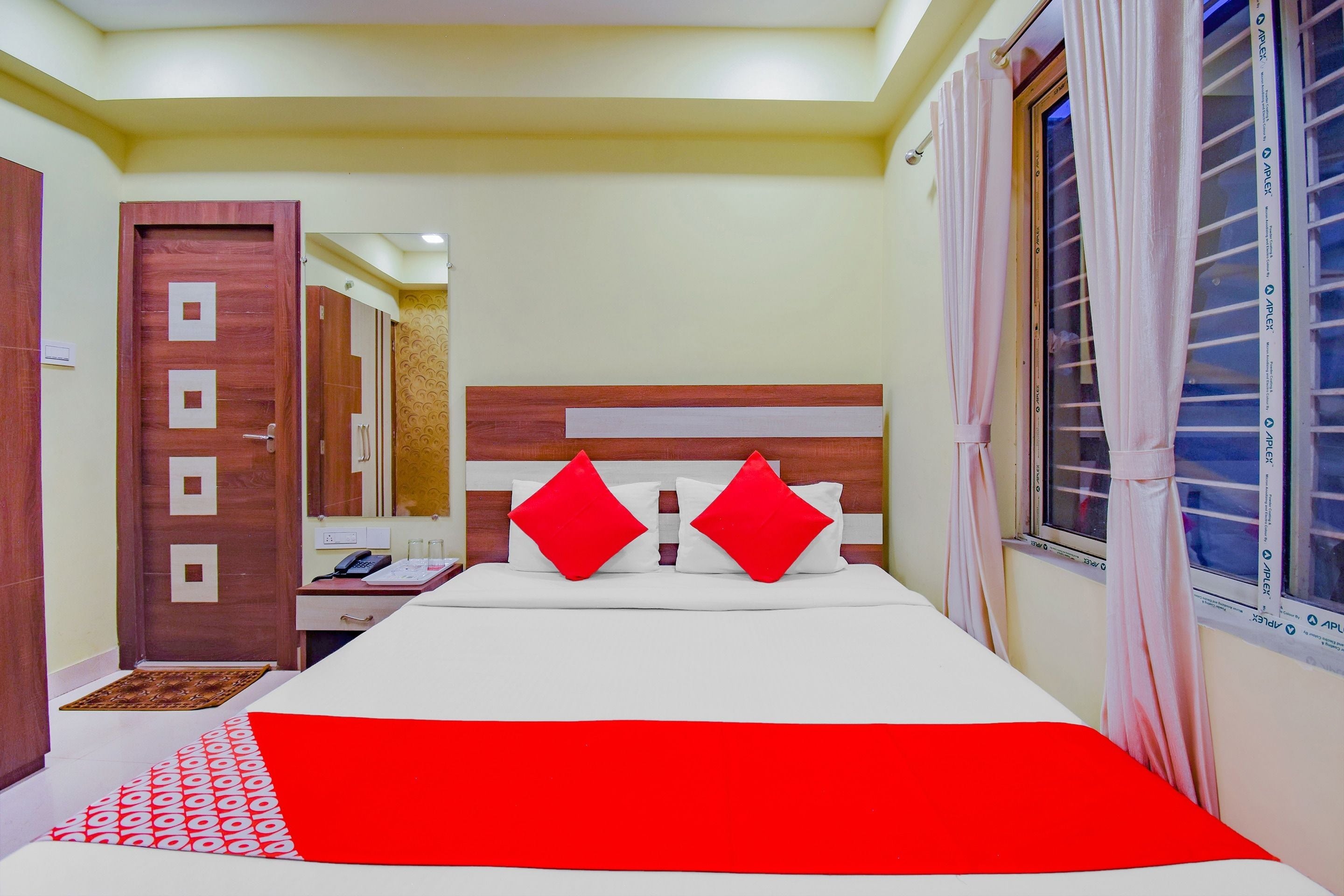 A hotel room with a bed, a desk, a mirror, and a window with curtains.