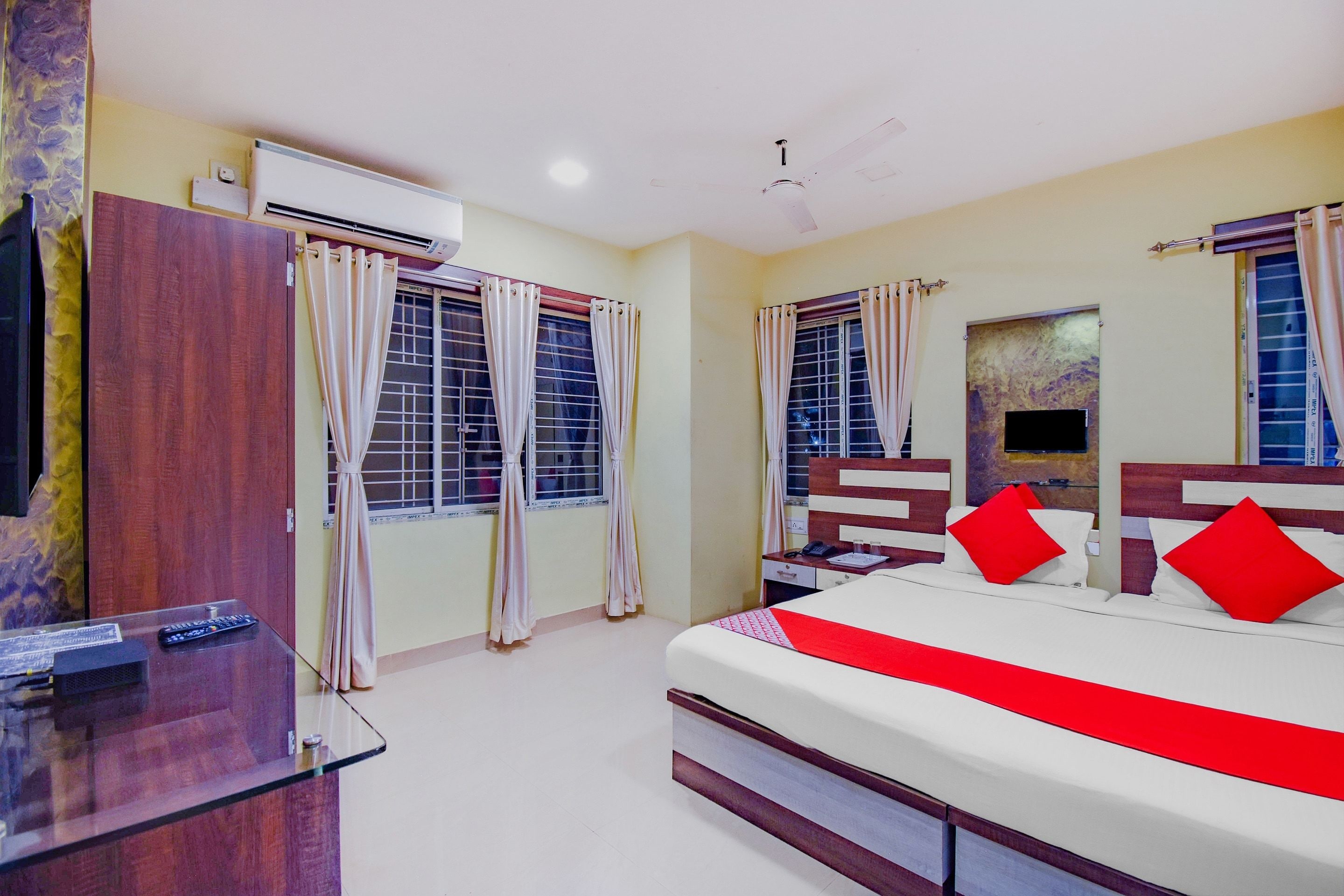 A hotel room with a bed, a desk with a telephone, and two windows with curtains.