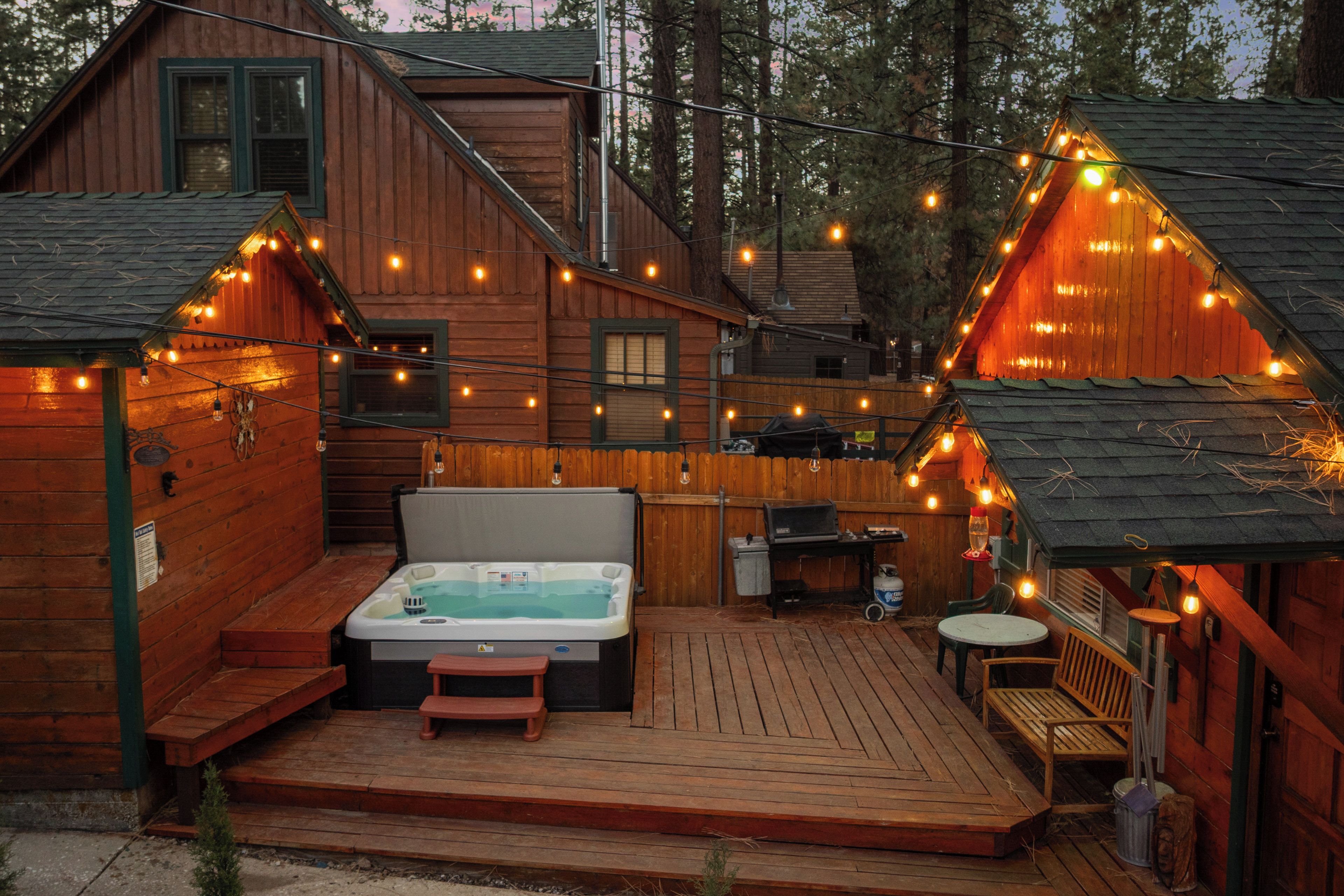 A wooden cabin with a hot tub, deck, and string lights.