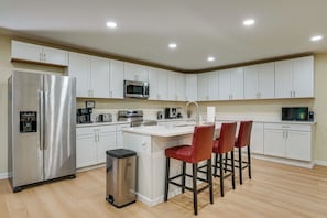 A modern kitchen with white cabinets, stainless steel appliances, a central island with bar stools, and a trash can. - Home Near Historic Dtwn! 3 Mi to Occoneechee Mtn (Hillsborough)