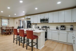 A modern kitchen with white cabinets, stainless steel appliances, and a wooden dining area with red chairs. - Home Near Historic Dtwn! 3 Mi to Occoneechee Mtn (Hillsborough)