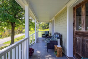A covered porch with a view of a road and trees, featuring a wicker chair and a small table. - Peaceful Farm House Near Catoctin Mtn Park (Myersville)