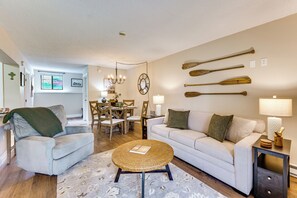 A living room with a sofa, armchair, coffee table, and a dining area with chairs and a table. - 10 Mi to Gunstock Resort! Condo Near Lake Access (Laconia)