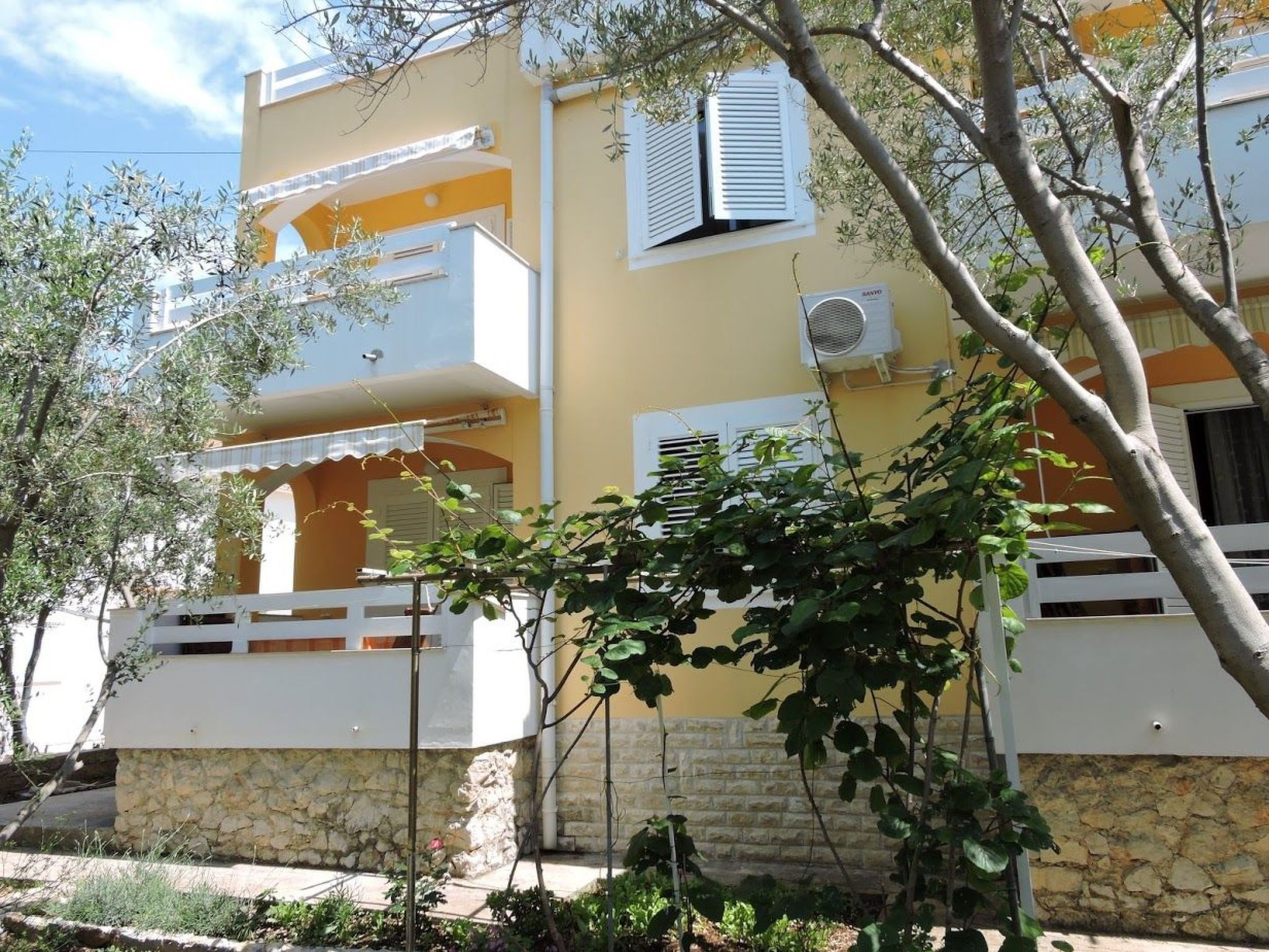 A two-story building with balconies, a stone base, and an air conditioning unit.