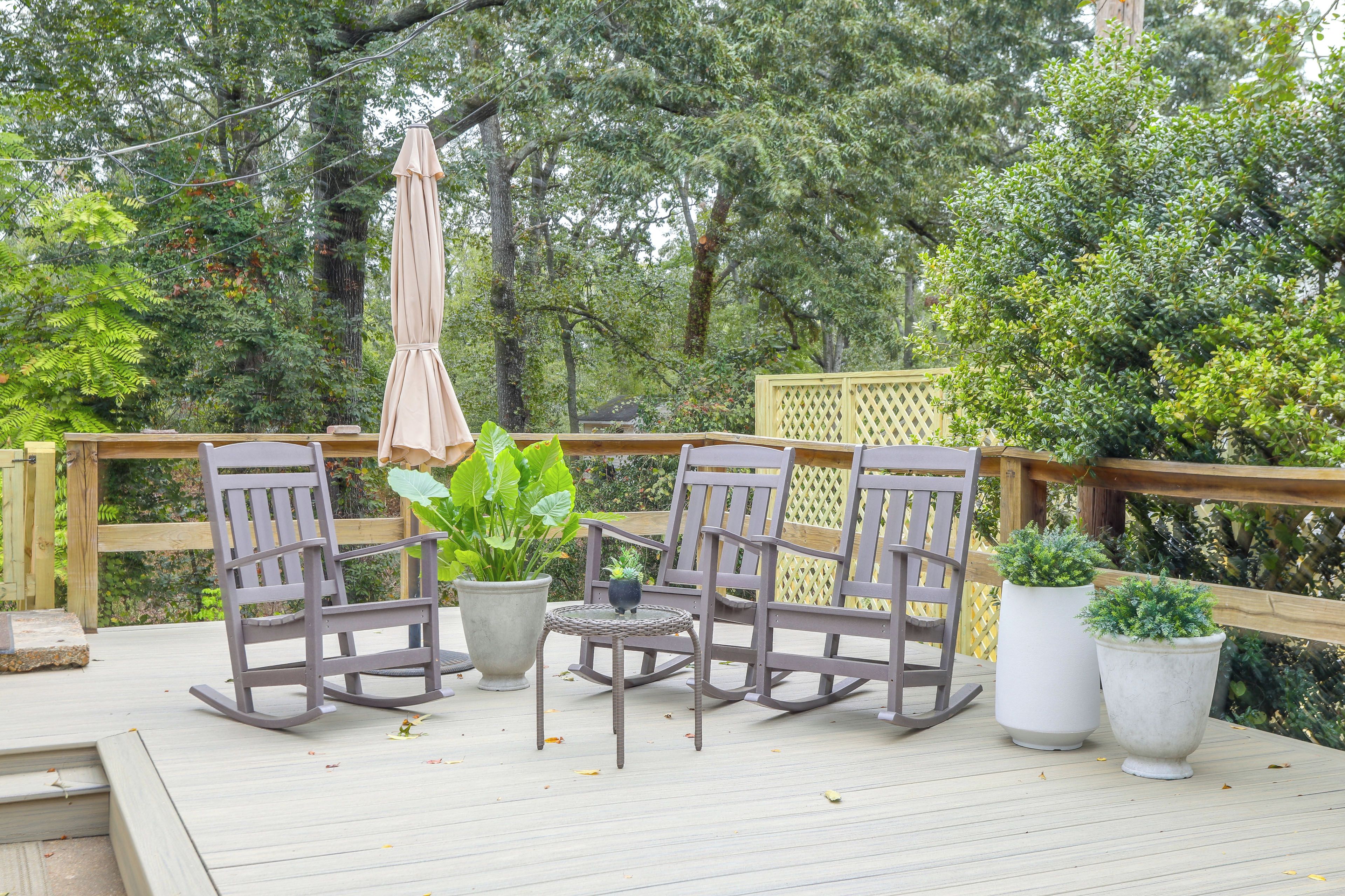 An outdoor patio with a wooden deck, two rocking chairs, a small table, and potted plants.