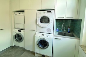A laundry room with stacked washers and dryers, a sink with a faucet, and a tiled floor. - 1 - House Windröschen (Borkum)