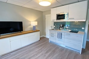 A modern kitchen with white cabinetry, a microwave, a sink, and a television on a wooden countertop. - 1 - House Windröschen (Borkum)
