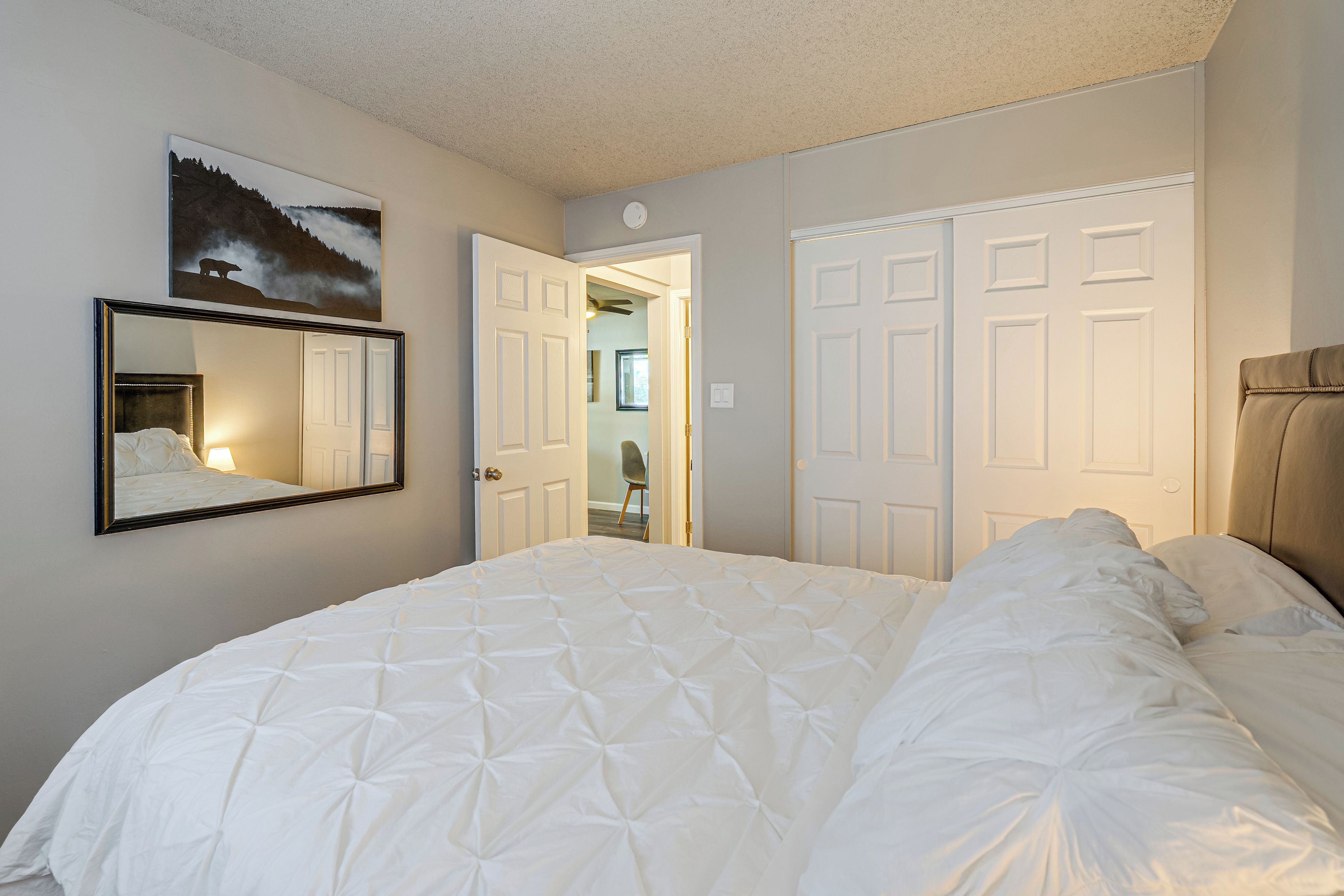 A hotel room with a large bed, a mirror, a door leading to another room, and a painting on the wall.